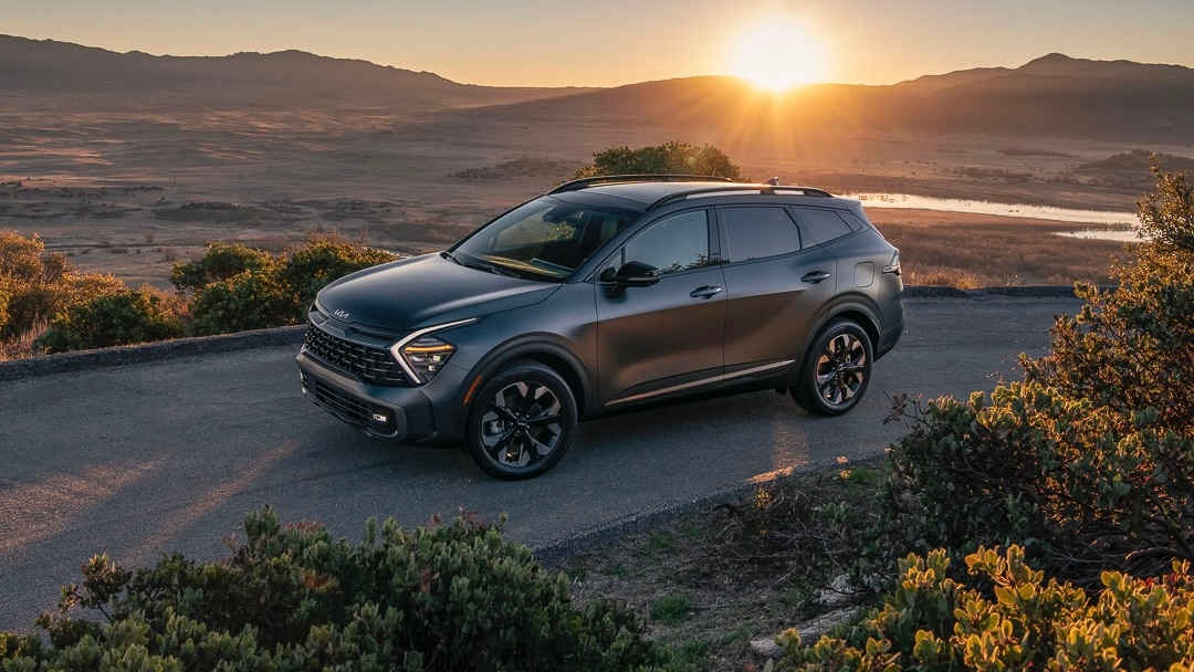 Une Kia Sportage PHEV stationné au coucher du soleil avec un paysage de montagne en arrière 