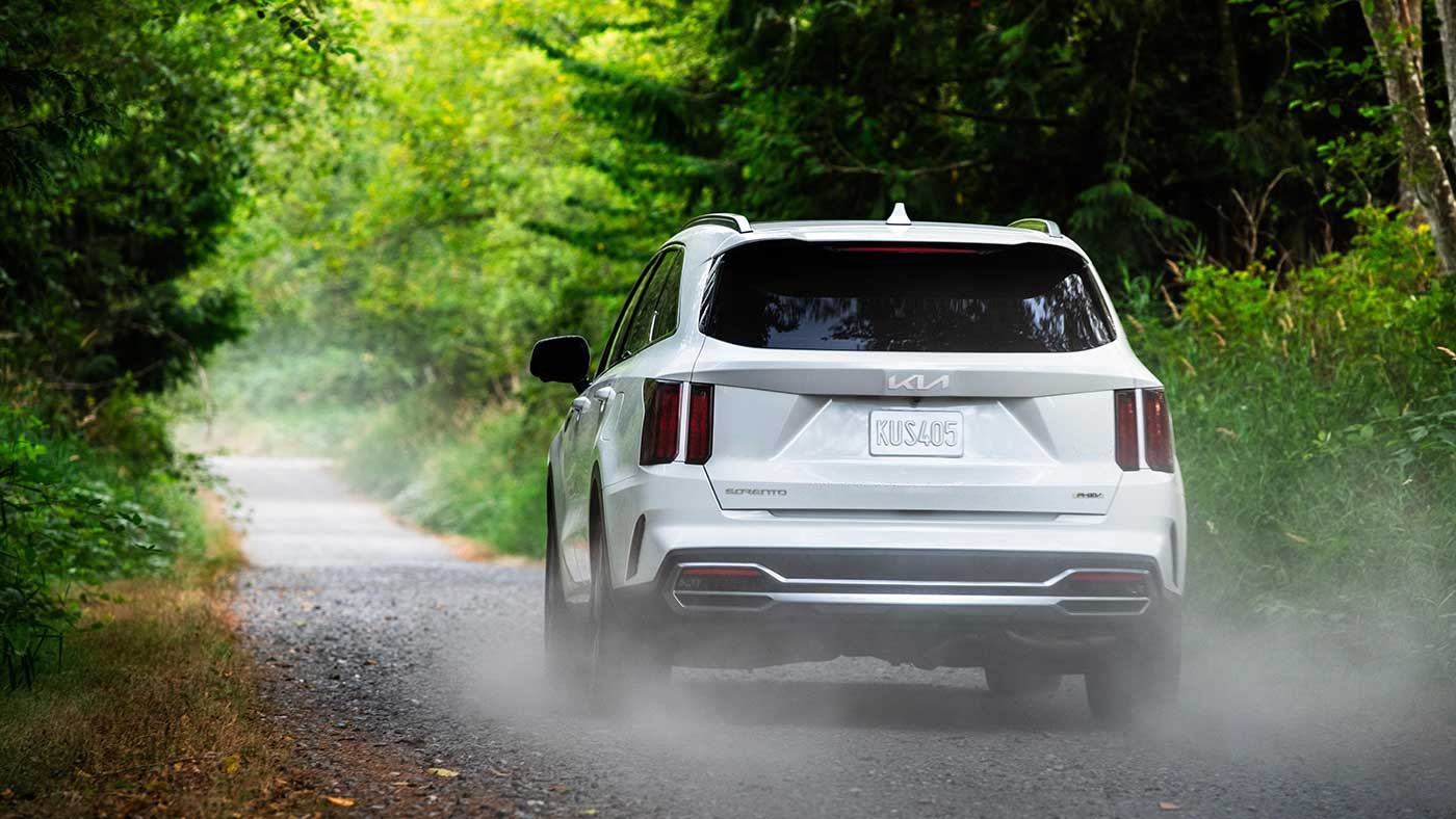 Vue arrière du Kia Sorento hybride PHEV 2024 roulant sur de la gravel en foret.